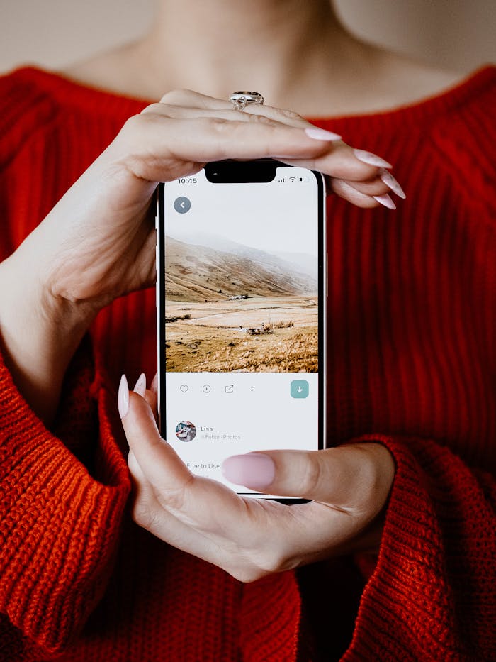Home A woman in a red sweater holds a smartphone displaying a scenic landscape image.