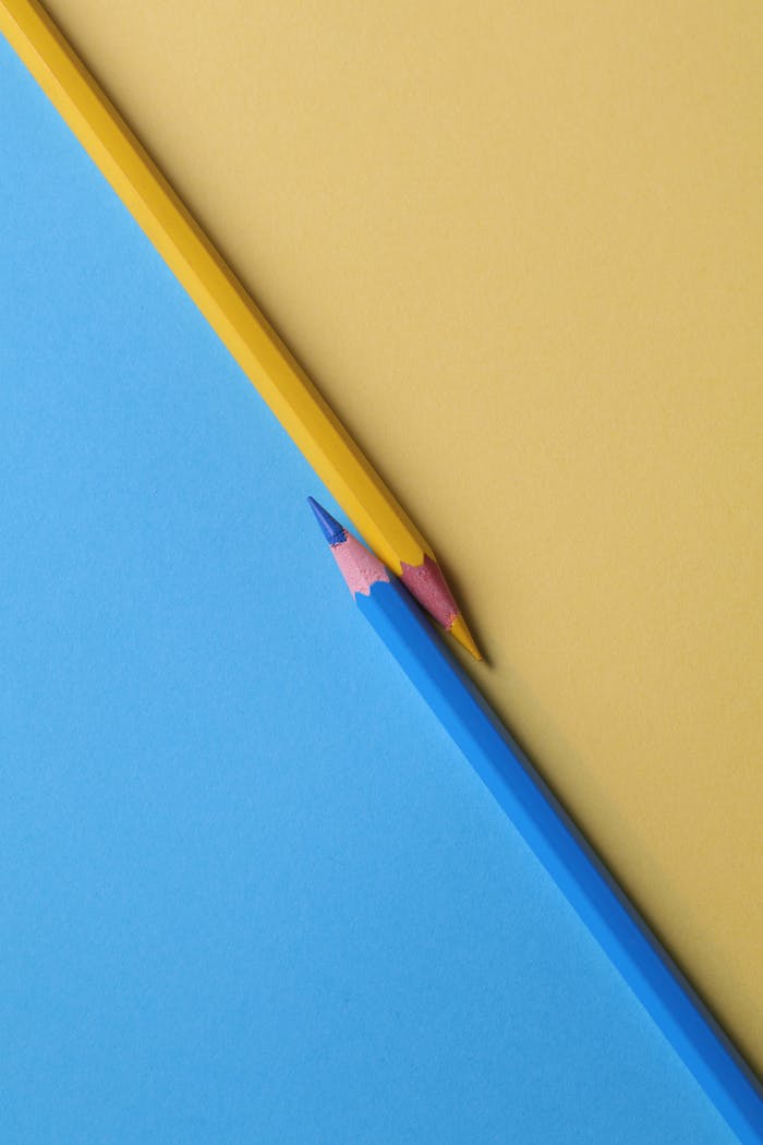 Home Close-up of vibrant yellow and blue colored pencils on contrasting paper backgrounds.